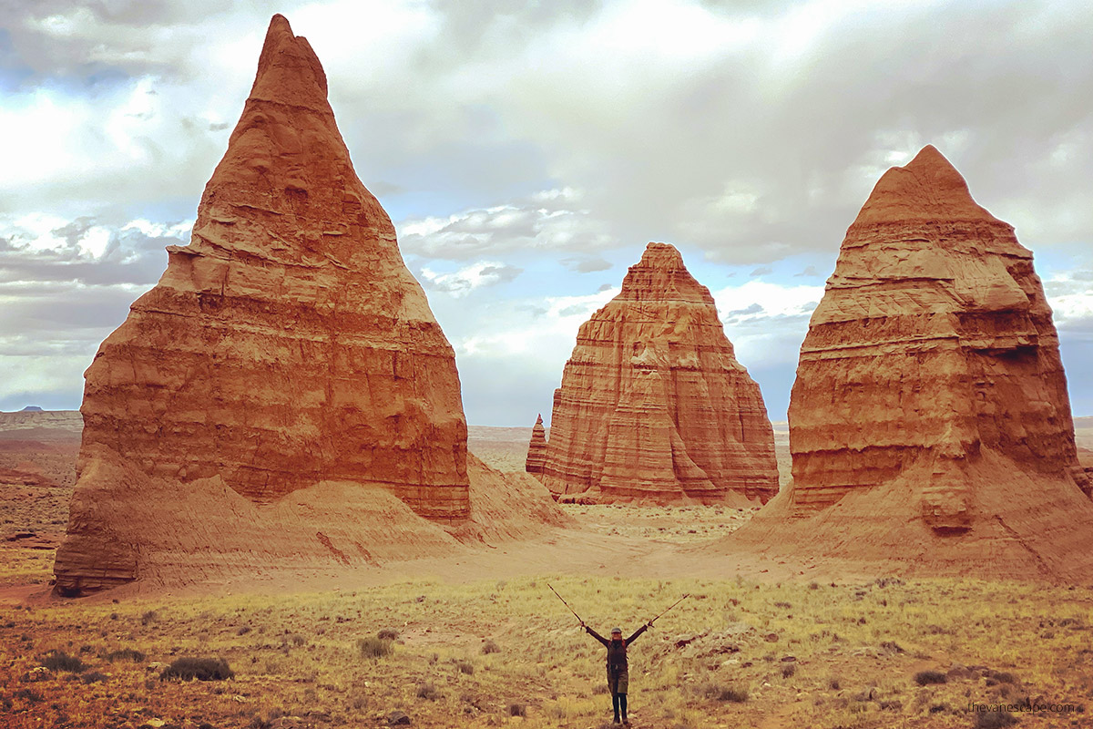 Agnes in Capitol Reef National Park standing like an orchestra conductor with trekking poles pointing to the mighty rocks of the temple of the sun and temple on the moon in rust and orange colors.