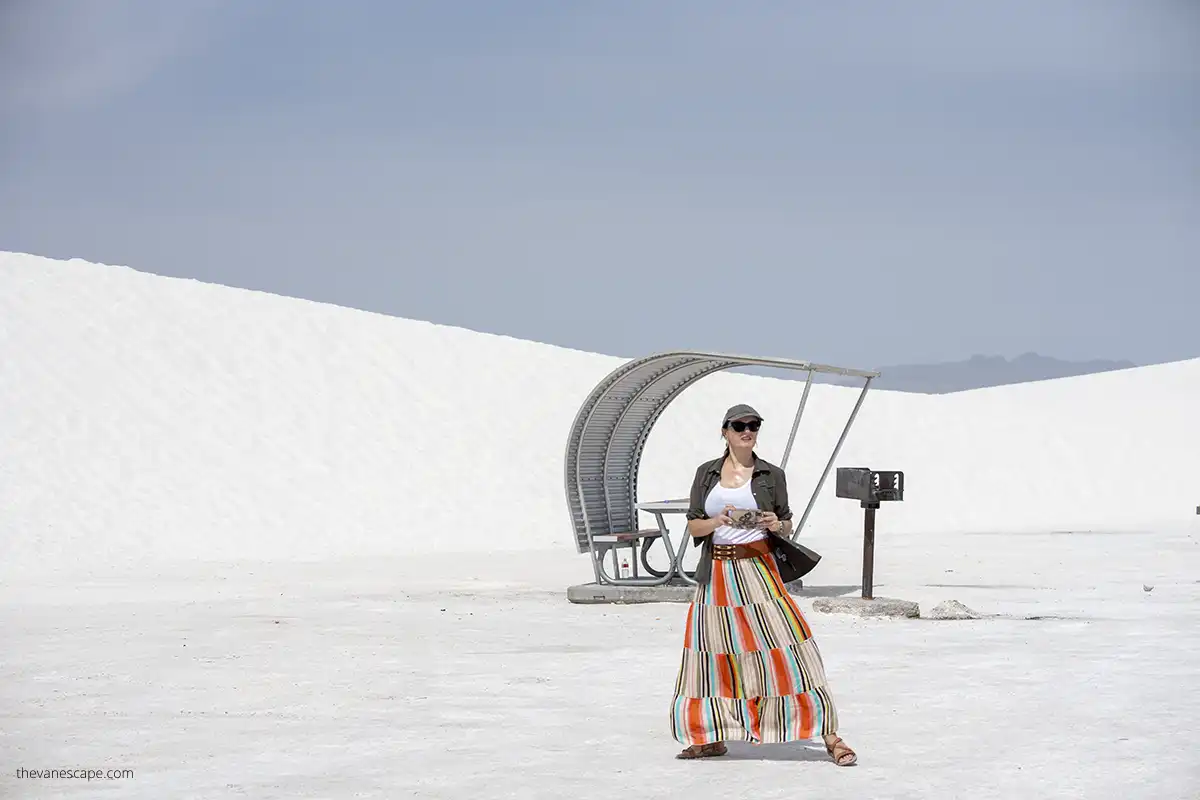 Agnes in orange skirt, sunglasses and hat taking pictures of white dunes. 