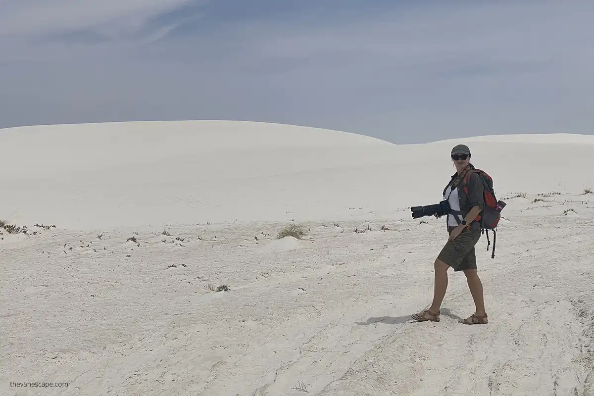 Agnes hiking in White Sand Dunes National Park wearing her backpack and camera with white dunes in the backdrop.