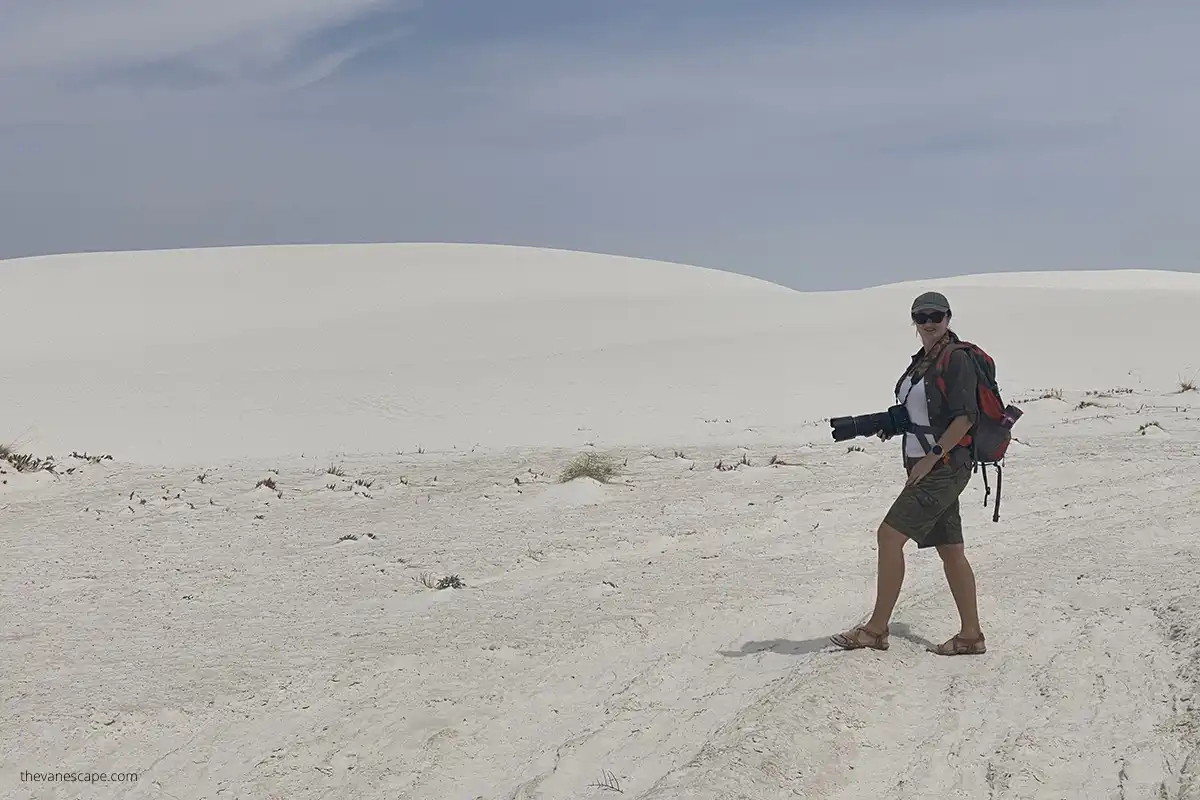 Agnes Stabinska, author, is hiking in White Sand Dunes National Park wearing her backpack and camera with white dunes in the backdrop.