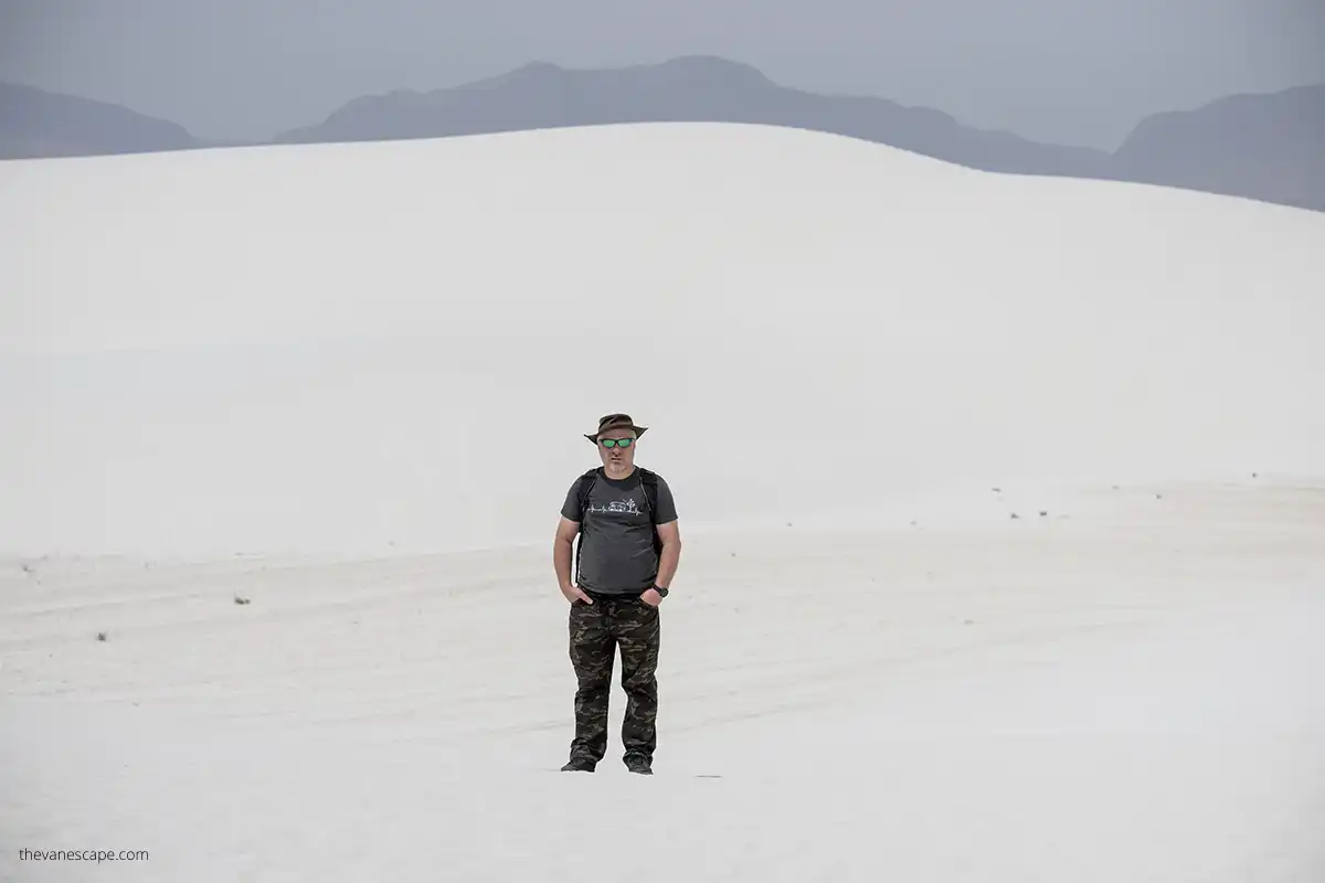 Chris hiking in White Sands National Park with huge white dune in a backdrop.