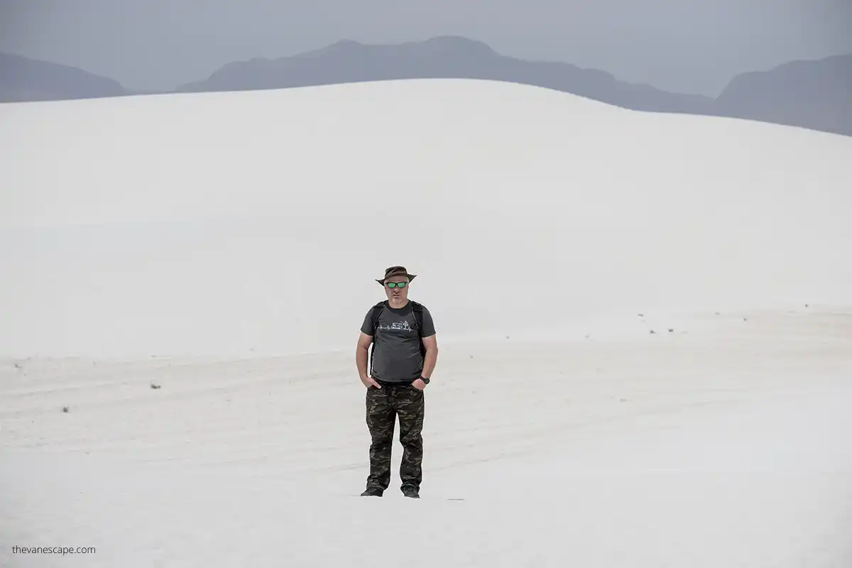 Chris is hiking in White Sands National Park with huge white dune in a backdrop.