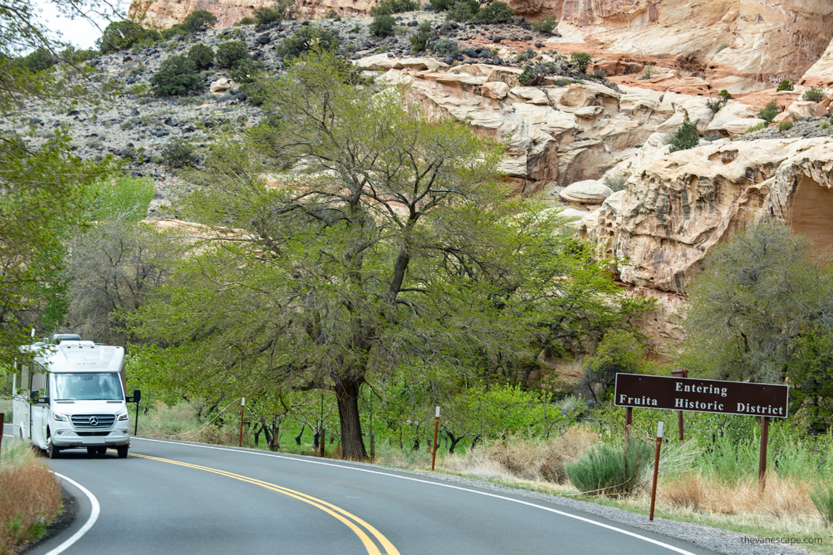 sign - entering fruita historic distric with becdrop of green trees and oranges rock and white RV on the road.