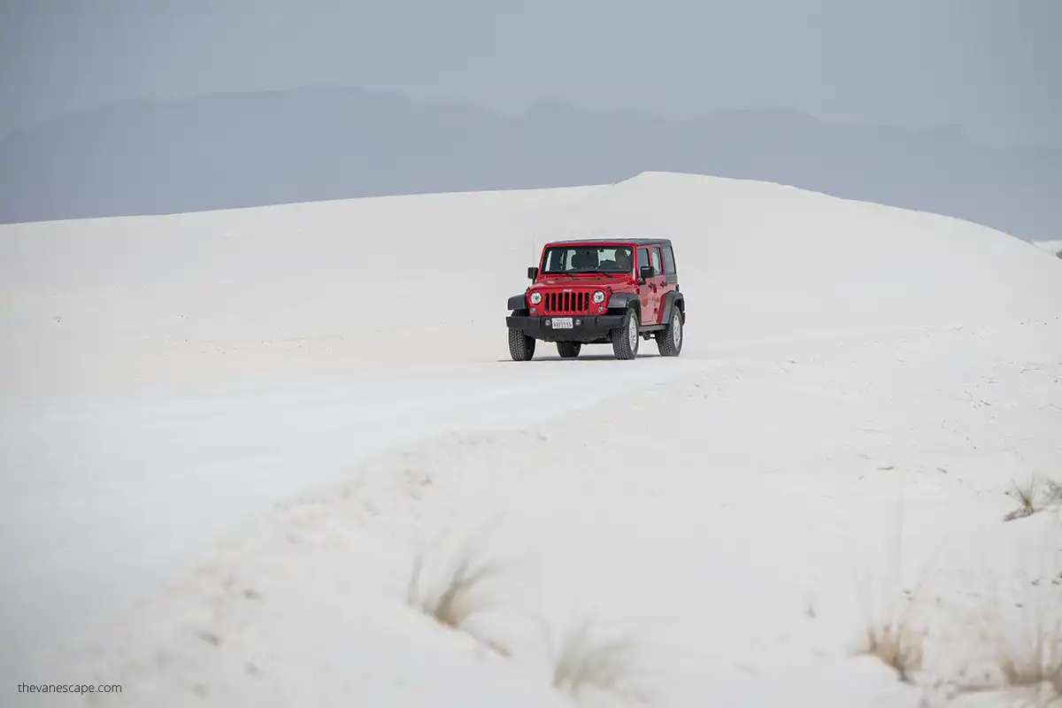 Chris driving in a red Jeep Wrangler on Dunes Drive road which is white due to the white sand on its surface.